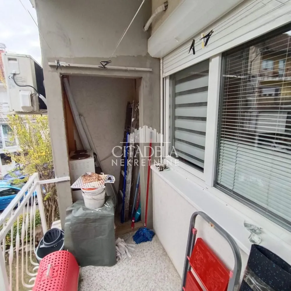 Manji balkon sa ostavom, klima uređajem i prozorom sa roletnama.
