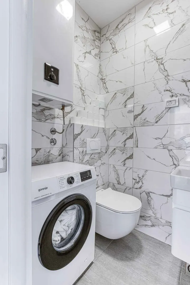 Smaller bathroom with marble-pattern tiles, toilet, washbasin, and washing machine.