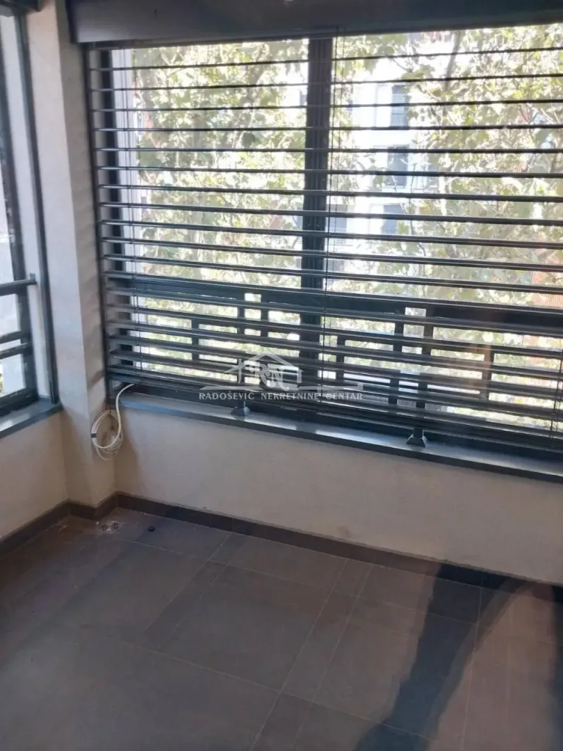 Zastakljena terasa sa roletnama na prozorima i popločanim podom.