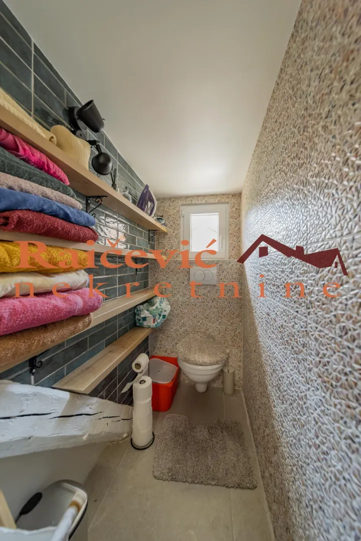 Manje kupatilo sa WC šoljom, drvenim policama i složenim peškirima.