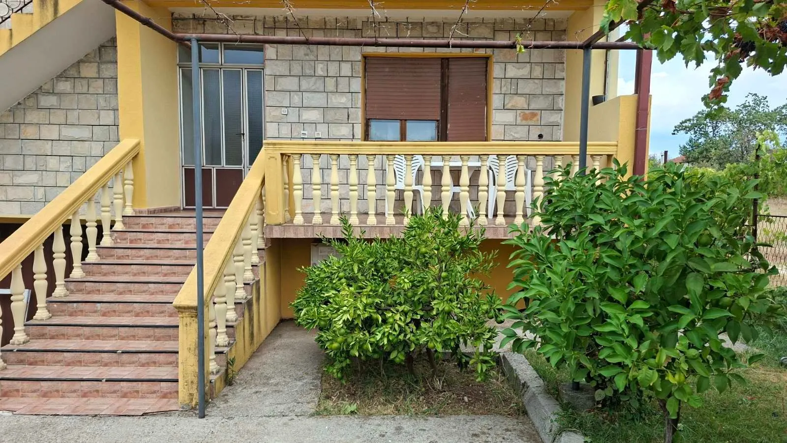 Pogled na spoljašnjost kuće sa stepeništem, terasom i uređenim dvorištem.