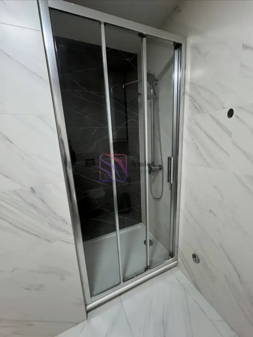 Moderna tuš kabina sa staklenim vratima u popločanom kupatilu.