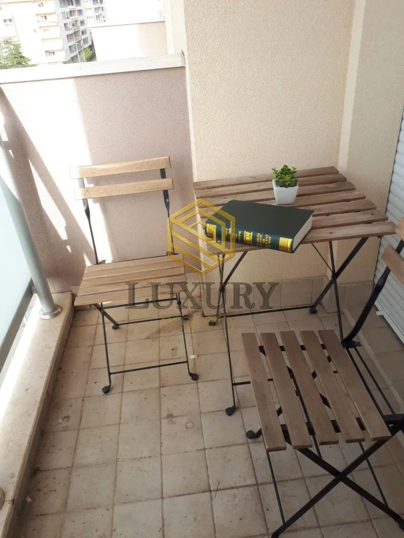 Manji namješteni balkonski prostor sa drvenim stolom i dvije stolice.