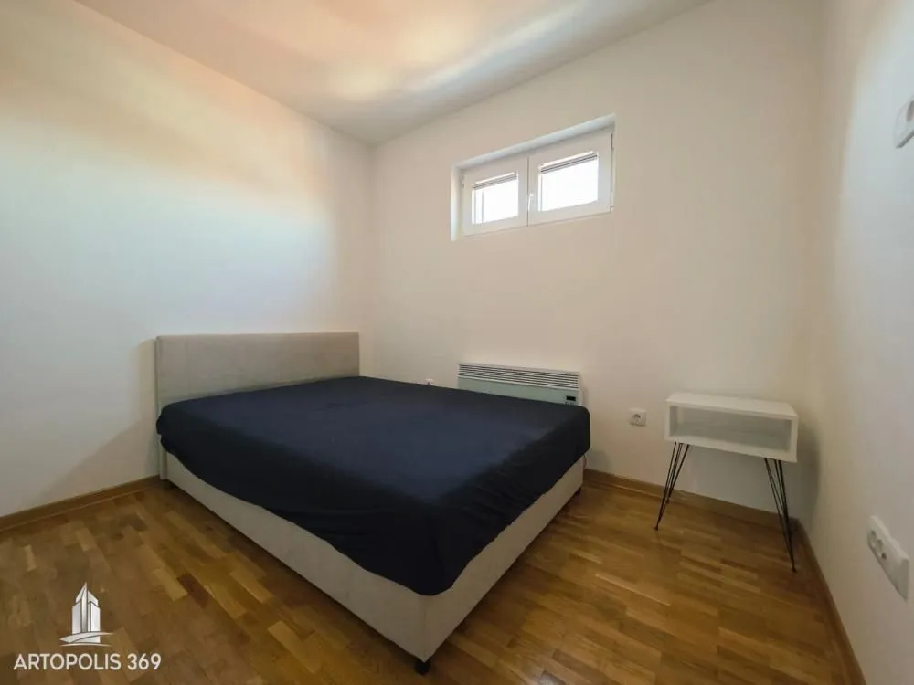 Small bedroom with a double bed, hardwood flooring, and a small window.