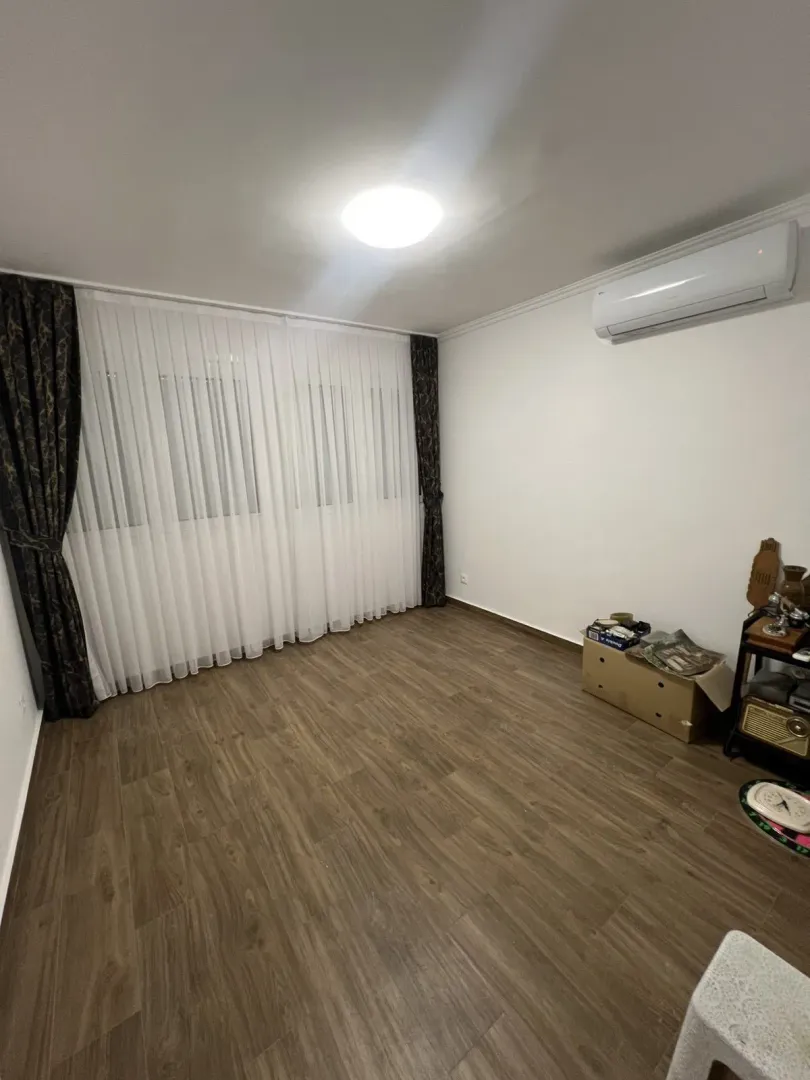 An empty room featuring laminate flooring, white curtains, and an air conditioning unit.