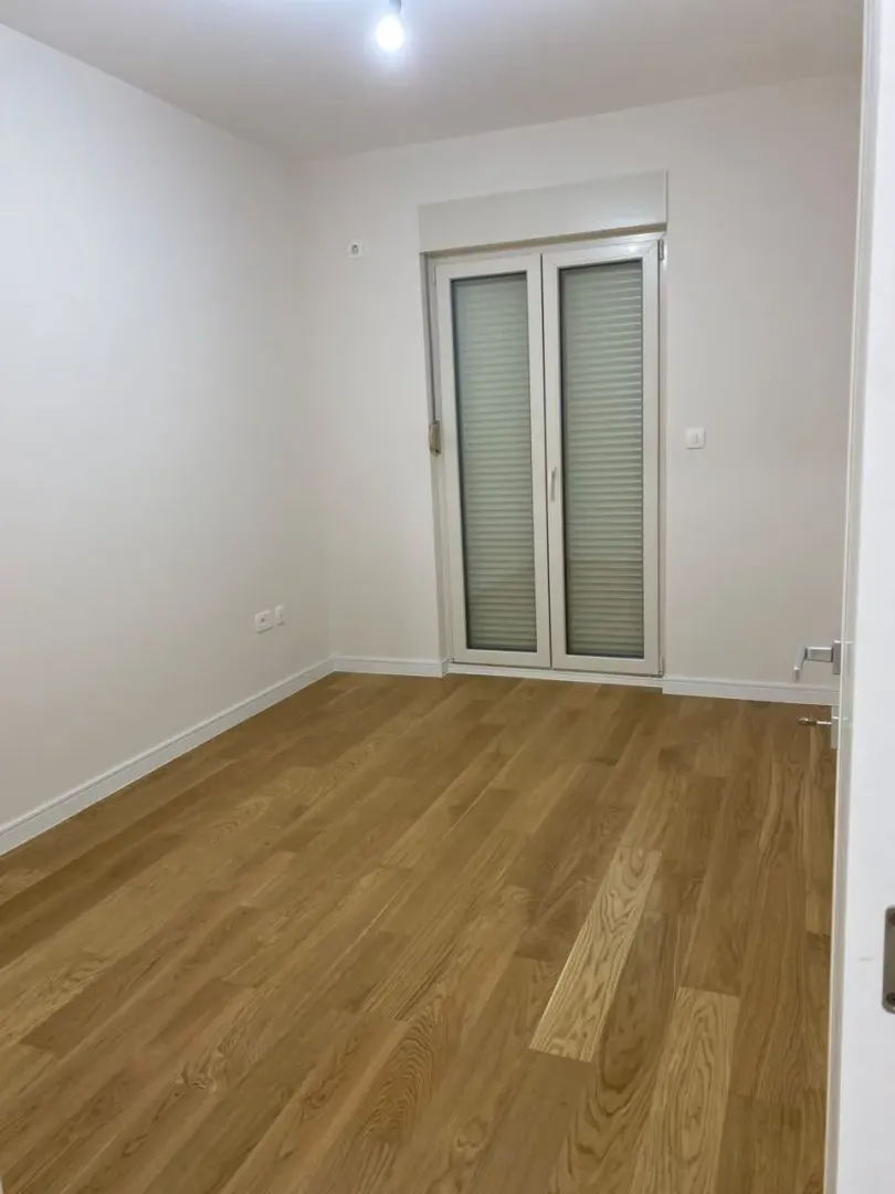Empty room with light wooden flooring and balcony doors.