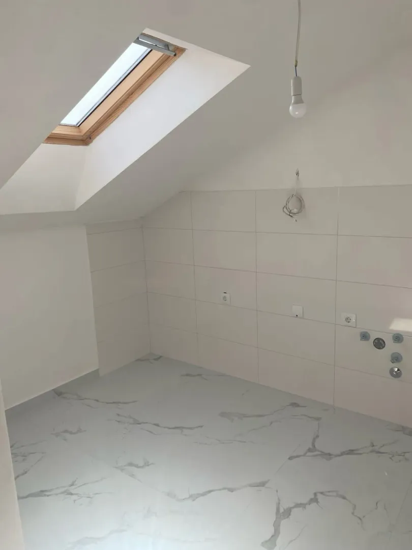 Nekorišćeno kupatilo u potkrovlju sa krovnim prozorem i keramičkim pločicama.