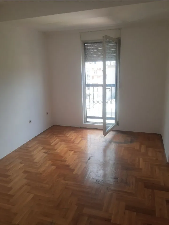 Prazna prostorija sa drvenim parketom i balkonskim vratima.