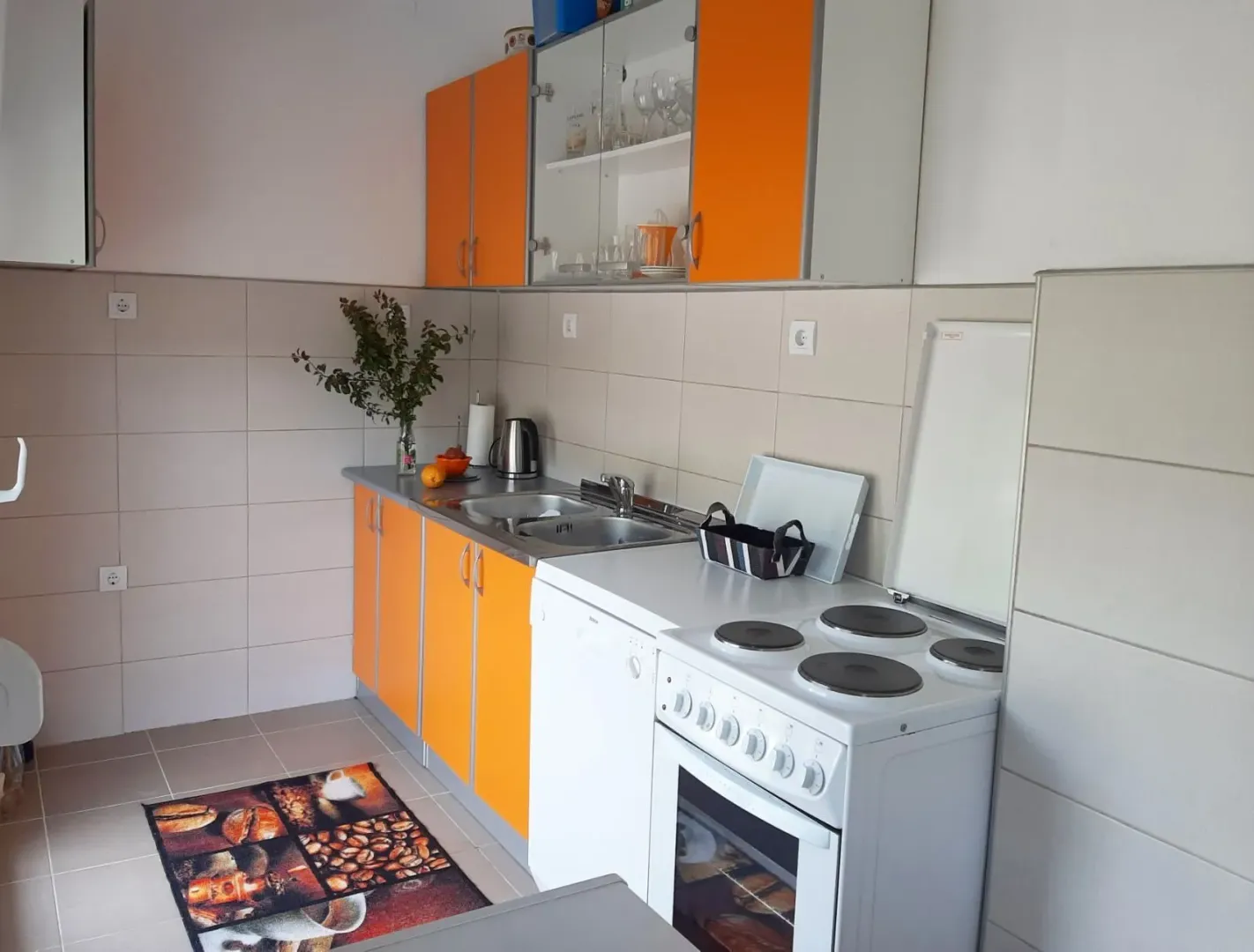 Manja kuhinja sa narandžastim elementima i bijelom šporetom.