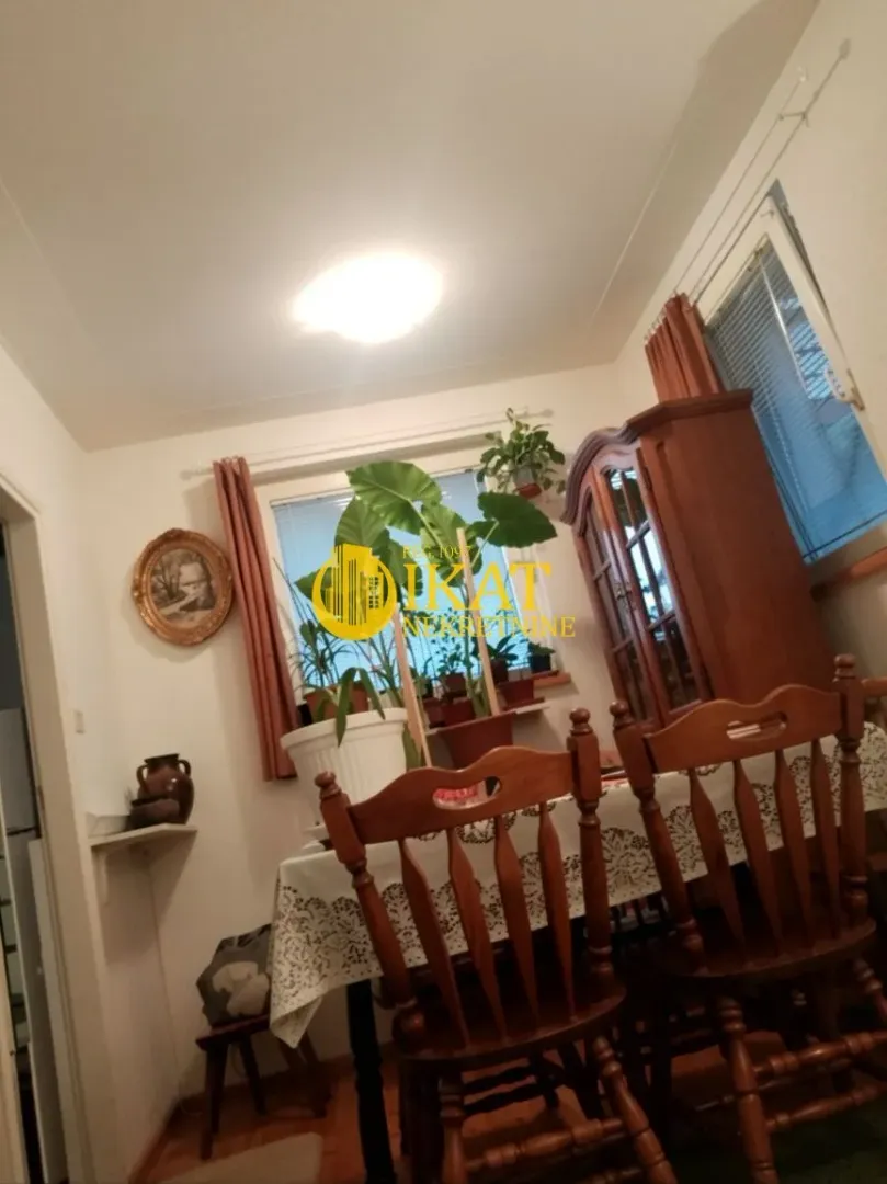 Trpezarija sa drvenim stolom, stolicama i vitrinom.