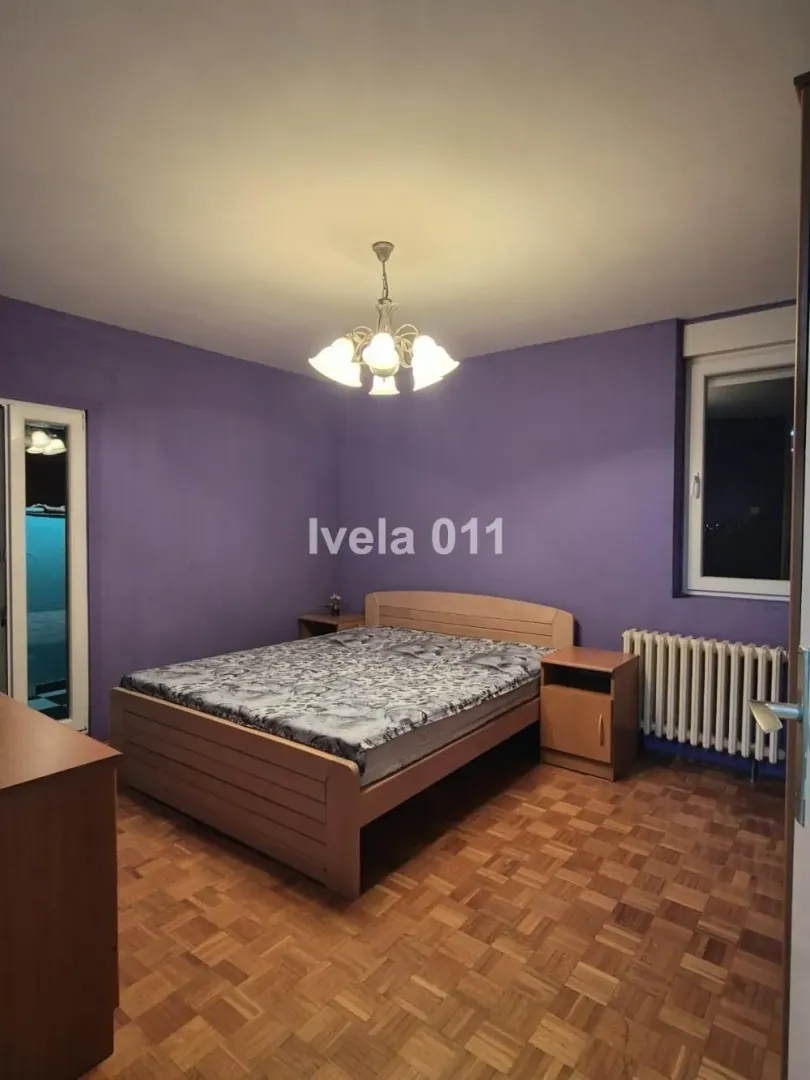 Furnished bedroom with a double bed, wooden parquet flooring, and purple walls.