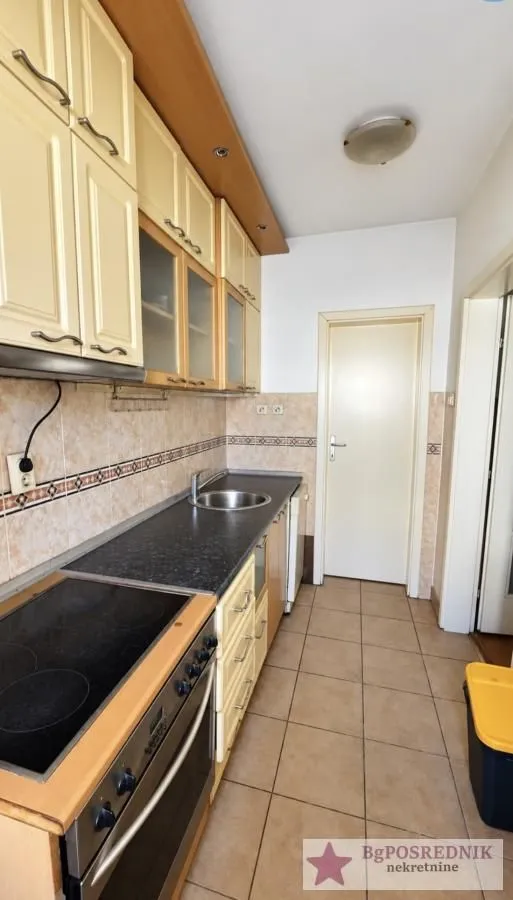 Long kitchen with light wood cabinets and ceramic floor tiles.