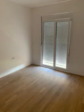 Prazna soba sa drvenim podom i balkonskim vratima sa roletnama. - image 2