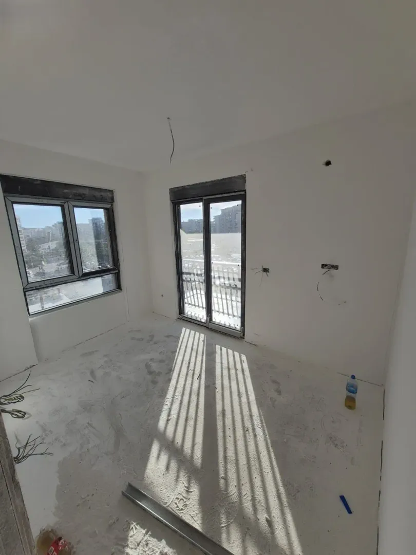 Empty room under construction with windows and balcony doors.