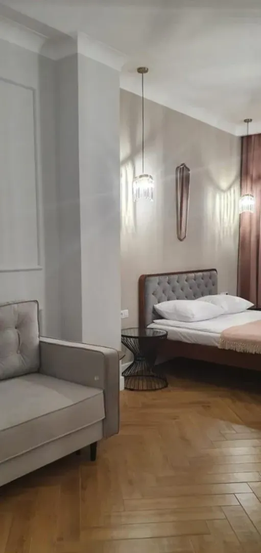 Moderna spavaća soba sa bračnim krevetom, foteljom i parketom na podu.