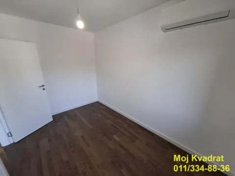 Prazna soba sa belim zidovima, tamnim parketom i klima uređajem. - image 6
