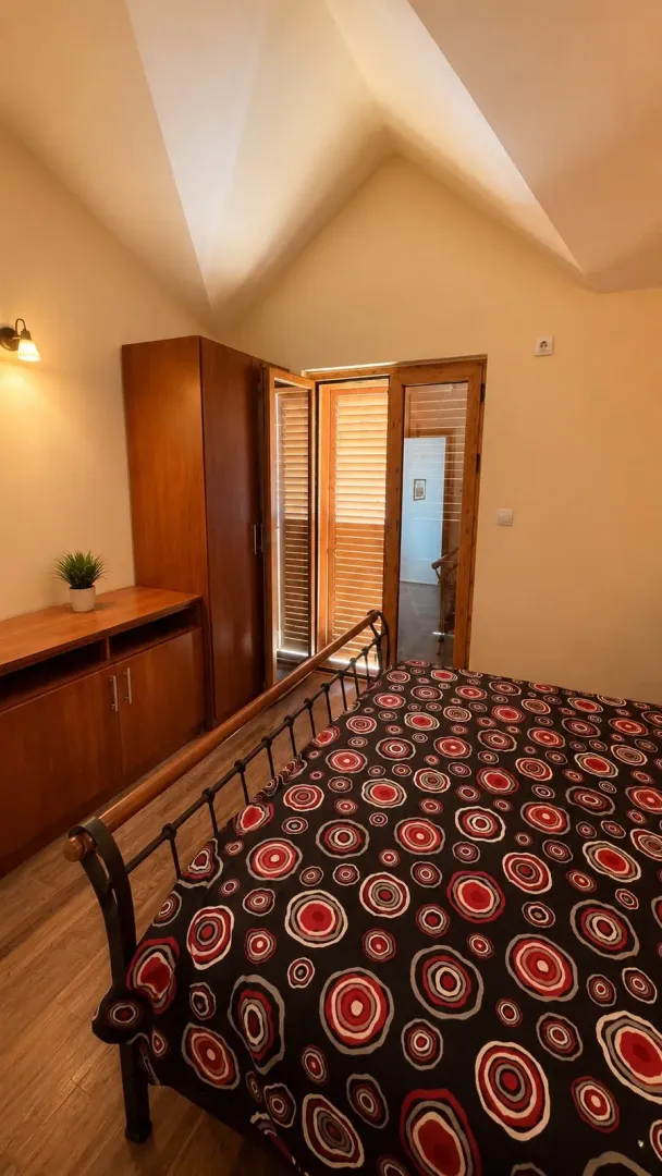 Spavaća soba sa bračnim krevetom, drvenim ormarom i izlazom na terasu.