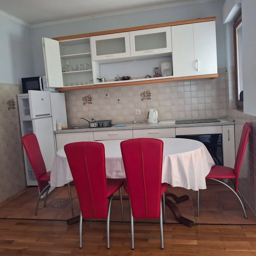 Kuhinja sa trpezarijskim stolom i crvenim stolicama.