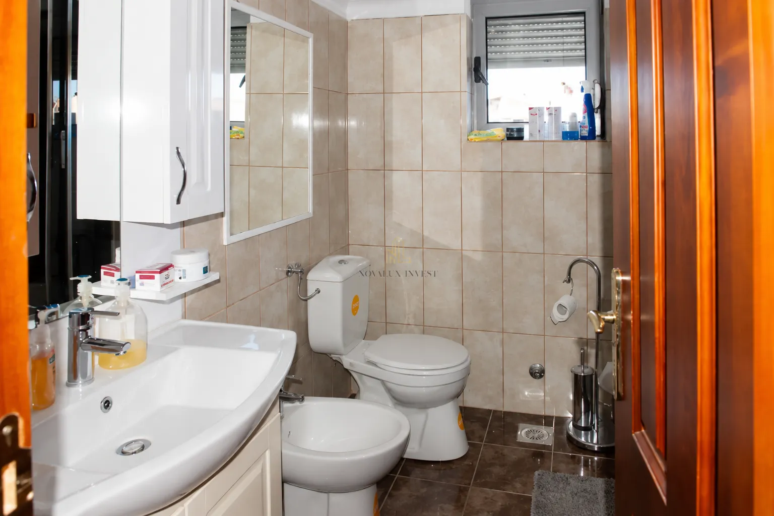 A compact bathroom with a washbasin, toilet, bidet, and tiled walls.