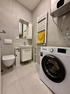 Modern bathroom with a shower, washbasin, toilet, and washing machine. - image 13