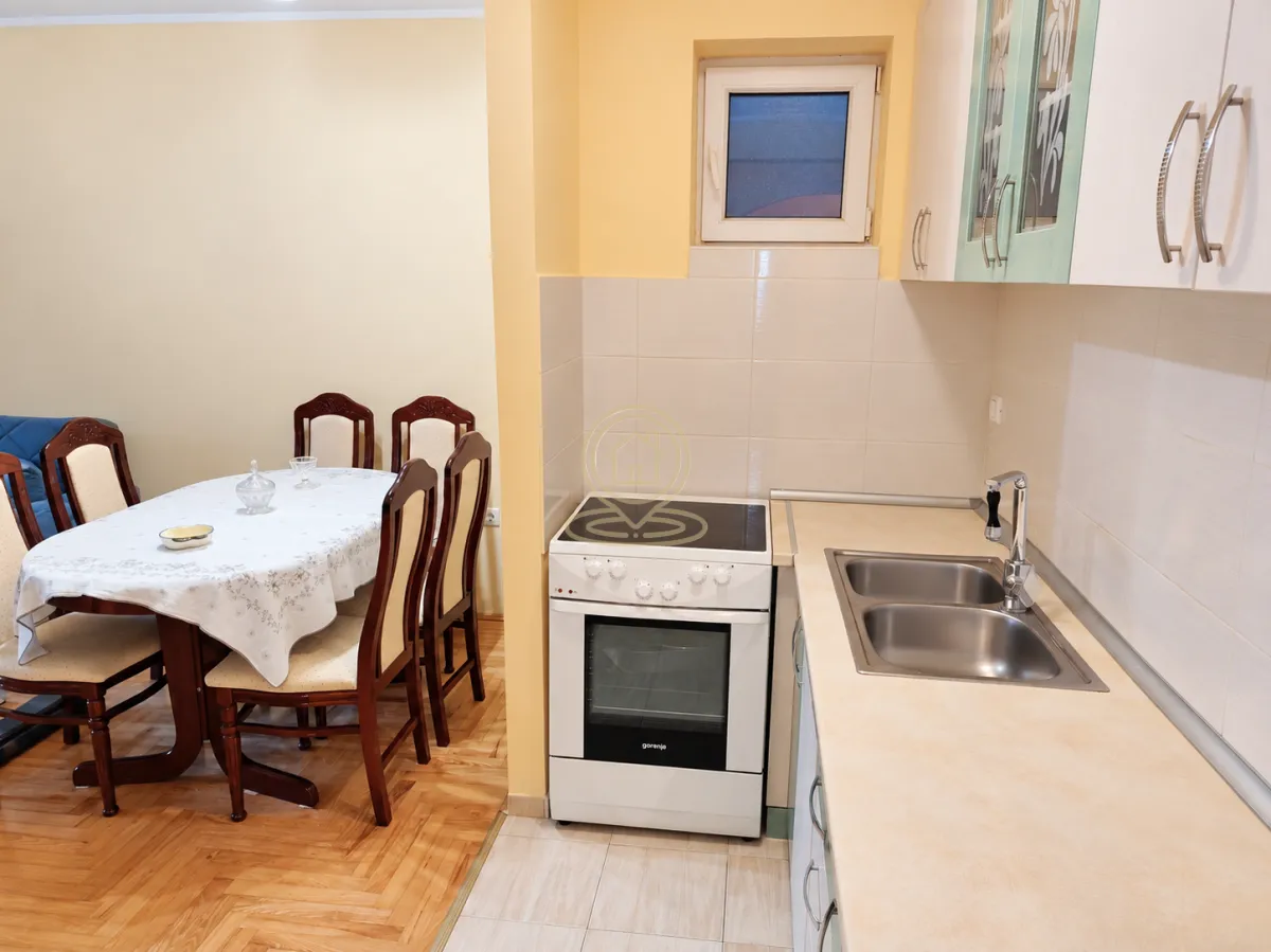 Kuhinja povezana sa trpezarijom sa drvenim stolom i stolicama.