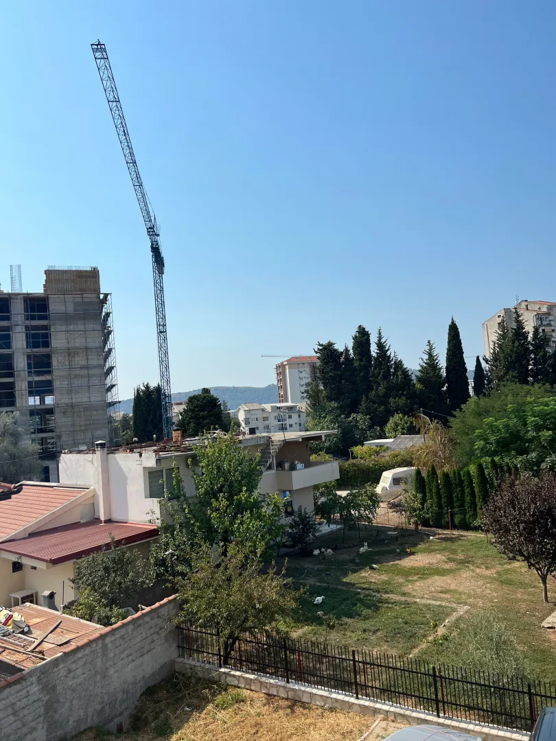 Pogled iz objekta na okolne zgrade, gradilište i zelenilo.