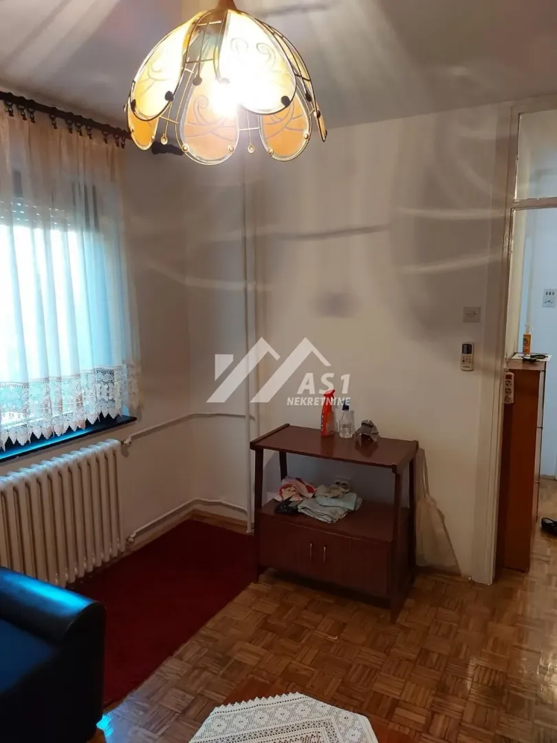 Manji deo dnevne sobe sa drvenim stočićem, radijatorom i lusterom.