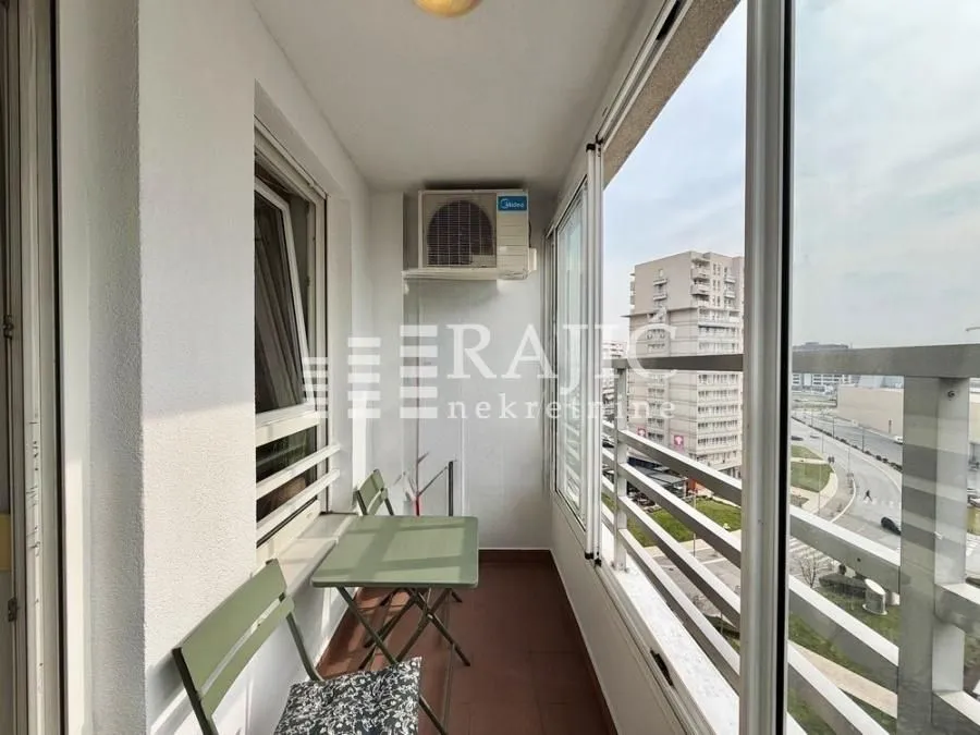 Enclosed balcony with seating furniture and a city view.