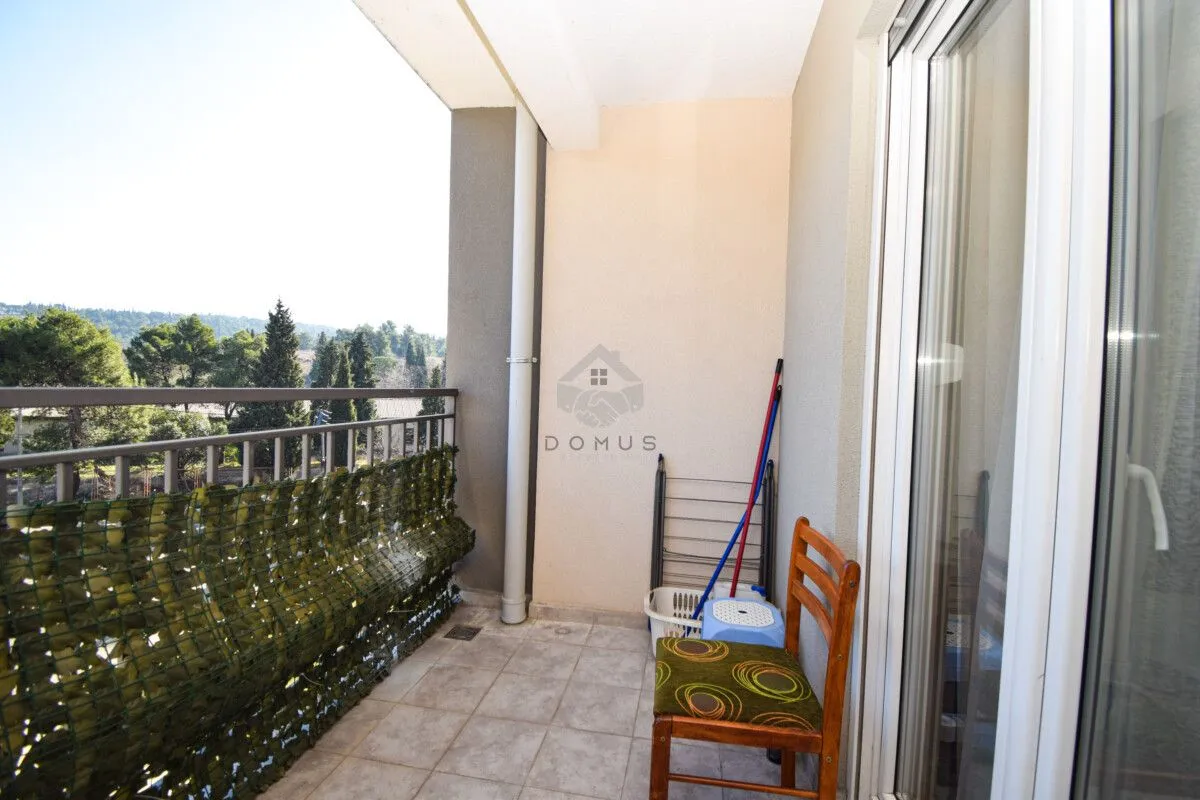 Covered balcony with a wooden chair, clothes drying rack, and nature view.