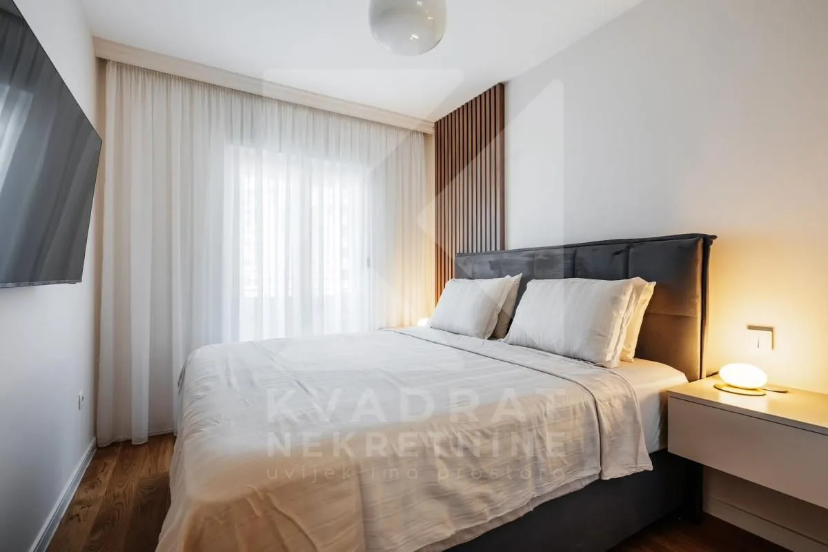 Modern bedroom with a double bed, wall-mounted TV, and decorative wooden panels.
