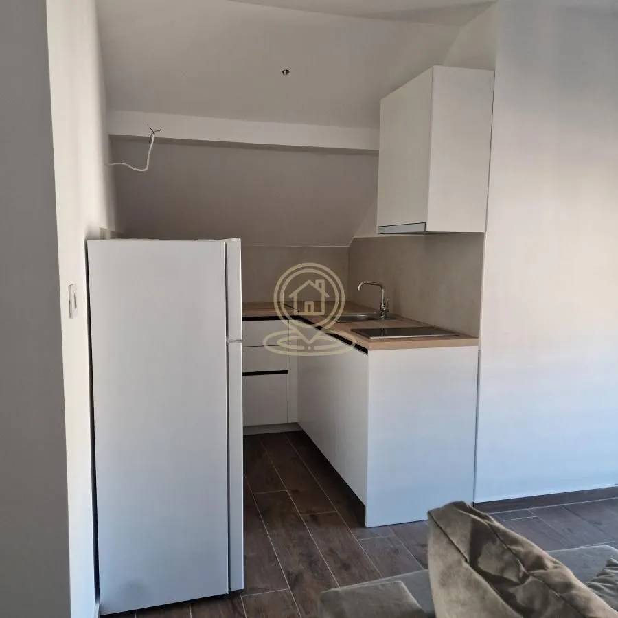 Small white attic kitchen with a refrigerator and built-in units.