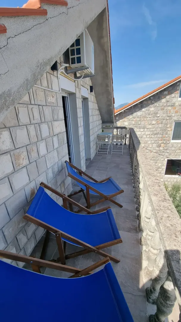 Dugačak popločani balkon sa kamenom fasadom i ležaljkama.