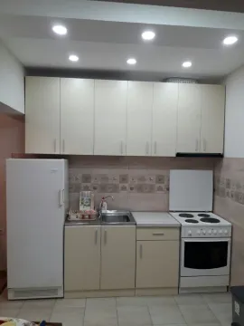 A simple kitchen with light-colored cabinets, a refrigerator, and a stove. - image 9