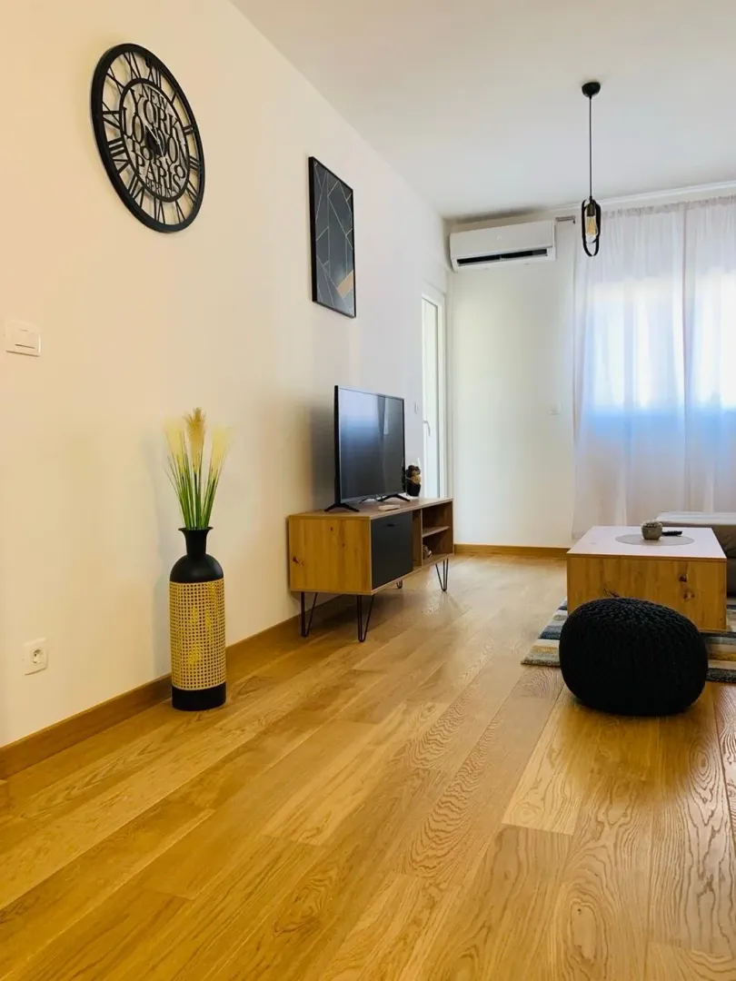 Svijetao dnevni boravak sa drvenim podom, TV komodom i dekorativnim elementima.