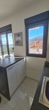 Manja kuhinja sa bijelim elementima i pogledom na okolinu kroz prozor. - image 14