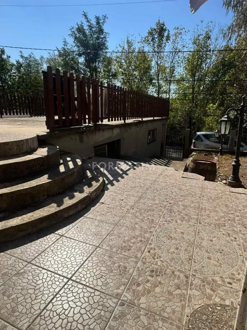 Dvorište sa popločanim platoom, stepeništem i drvenom ogradom ispred kuće.