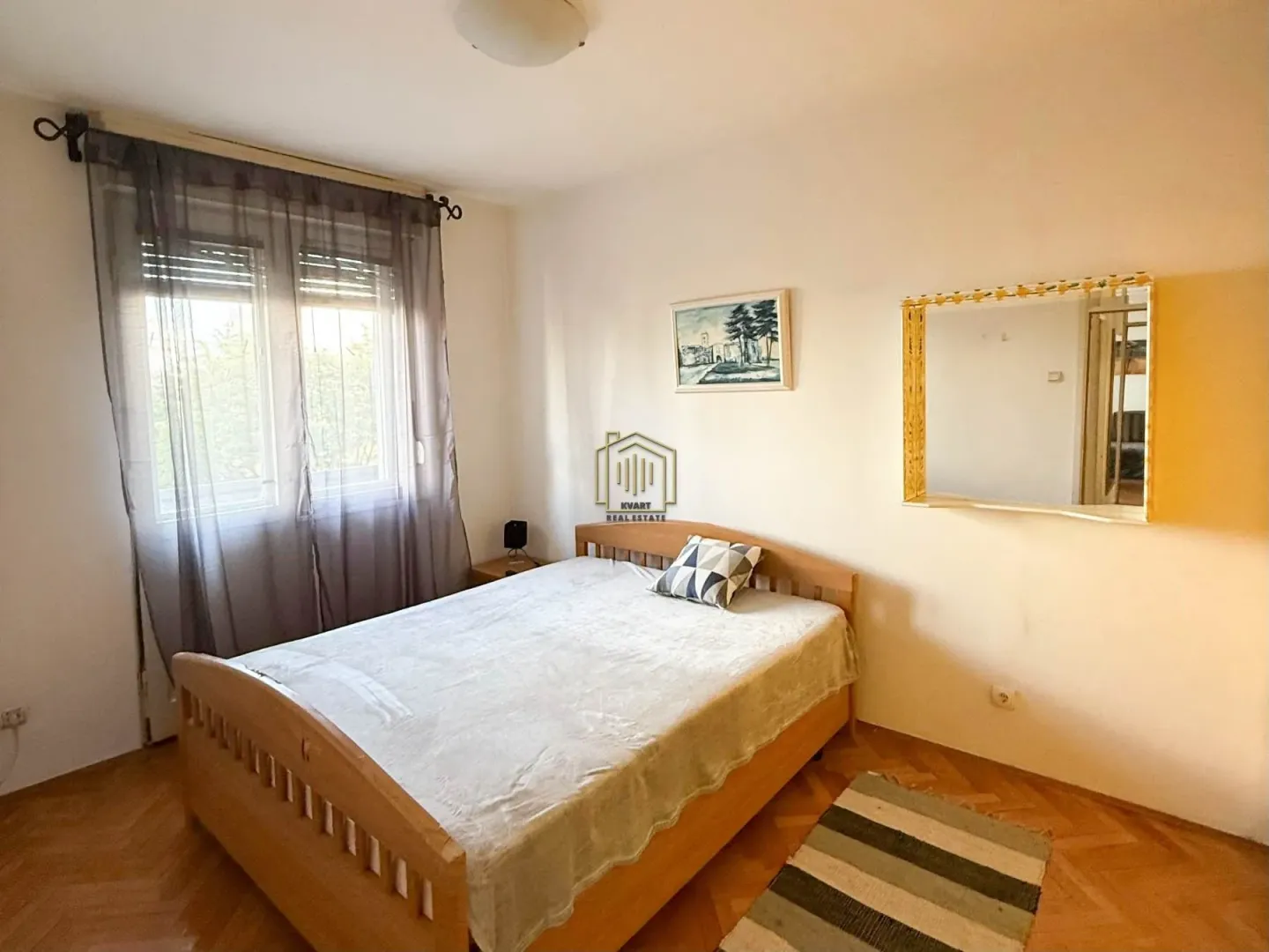 Spavaća soba sa bračnim krevetom, prozorom i ogledalom na zidu.