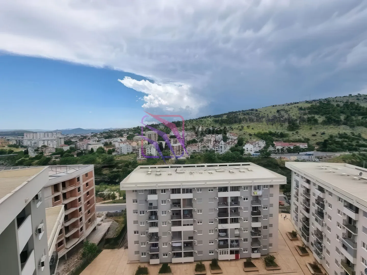 Pogled sa prozora na okolne zgrade i brda u daljini.