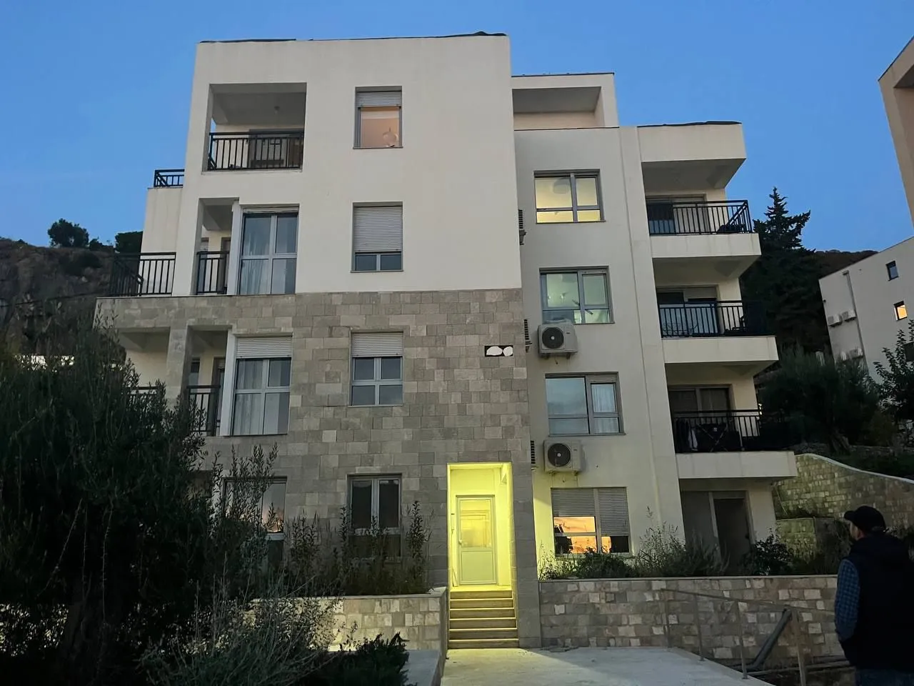 Spoljašnji izgled moderne stambene zgrade sa terasama u sumrak.