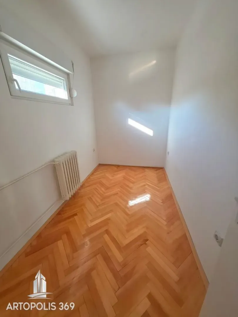Prazna svetla soba sa parketom i radijatorom.
