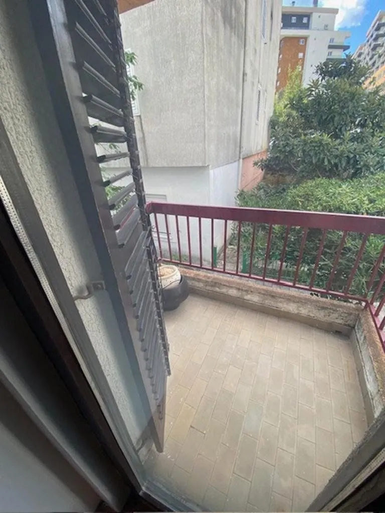 Small tiled balcony with a red railing and a view of greenery.