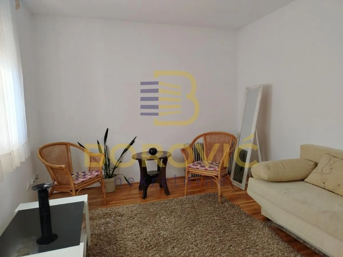 Dnevna soba sa garniturom, foteljama od pruća i drvenim podom.