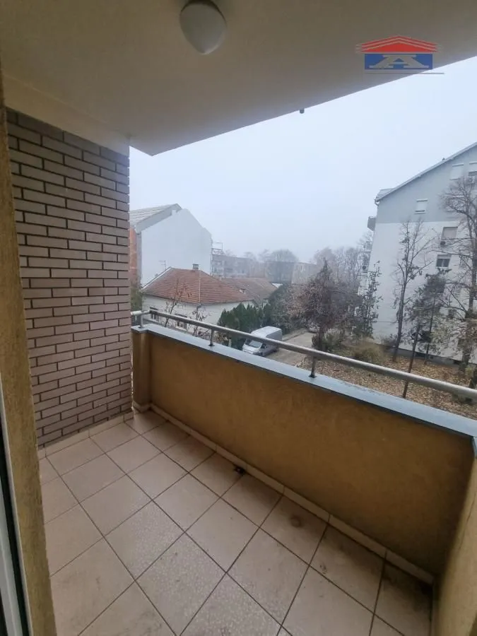 Natkriveni balkon sa popločanim podom i pogledom na okolne zgrade.