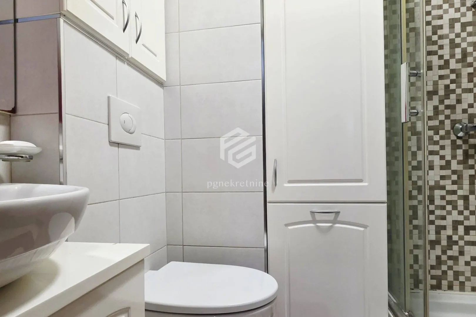 Smaller bathroom with white cabinets, a washbasin, and a shower cabin.
