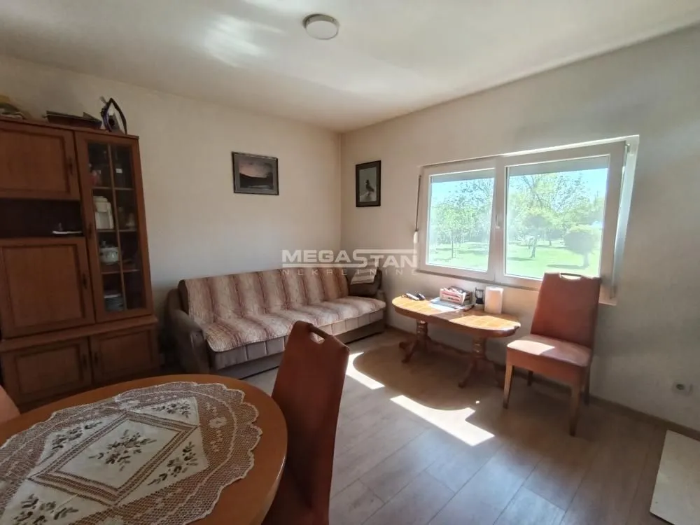 Living room with a sofa, dining table, and a window overlooking greenery.
