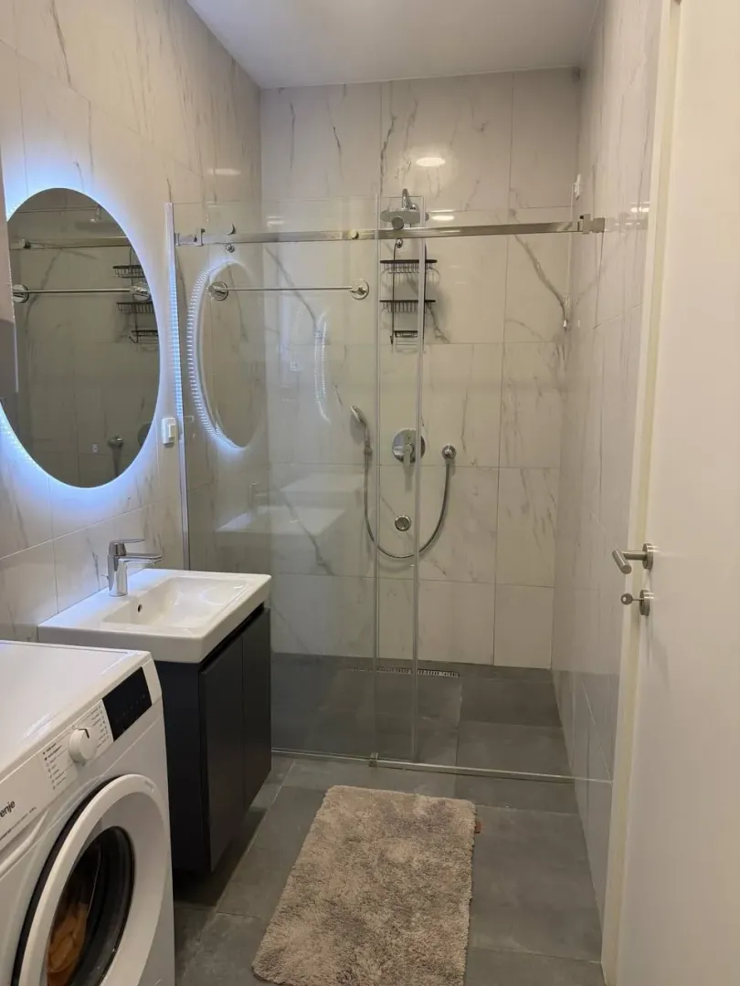 Modern bathroom with a walk-in shower, washbasin, and washing machine.