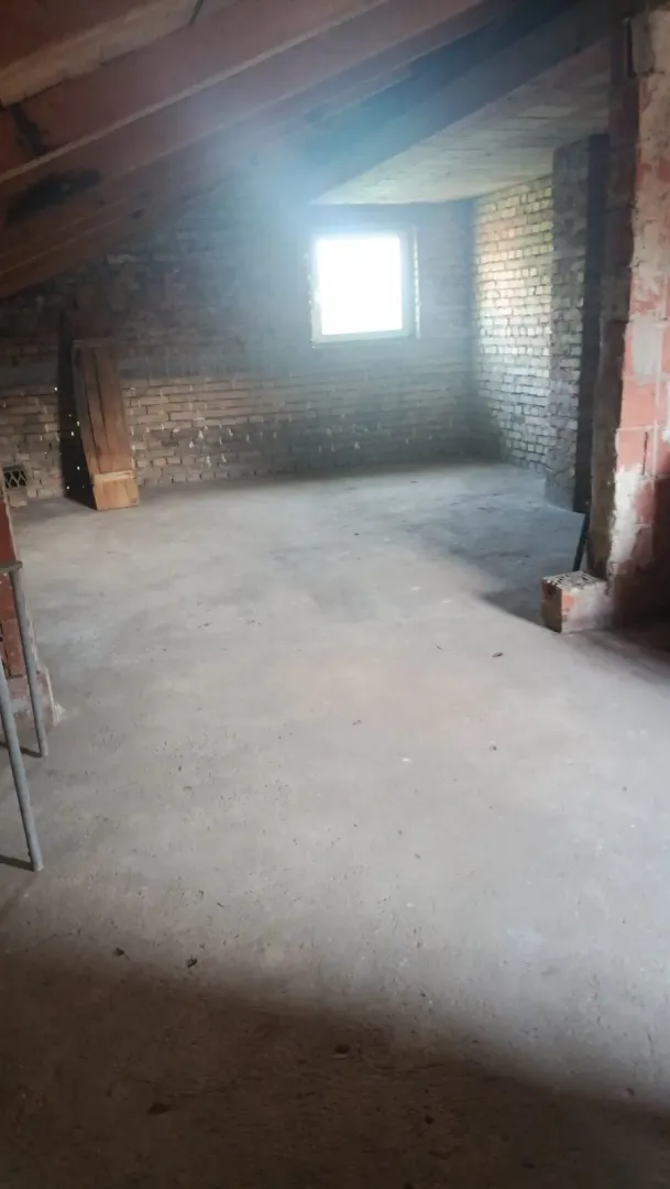 Potkrovlje u sivoj fazi izgradnje sa prozorom i kosim drvenim krovom.