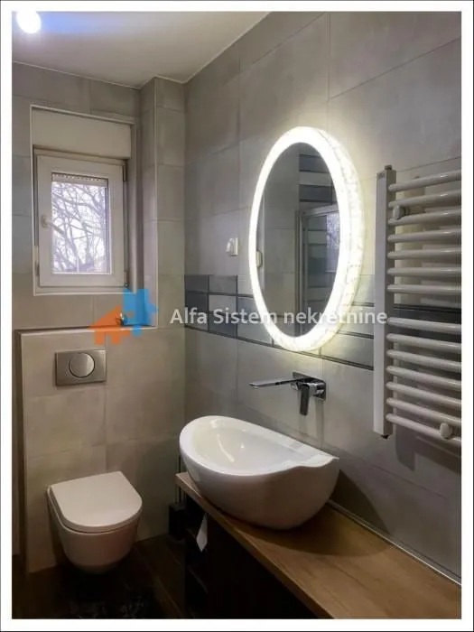 Modern bathroom with a washbasin, wall-hung toilet, and illuminated mirror.