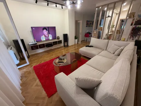 Prostrana dnevna soba sa ugaonom garniturom, crvenim tepihom i TV-om. - image 5