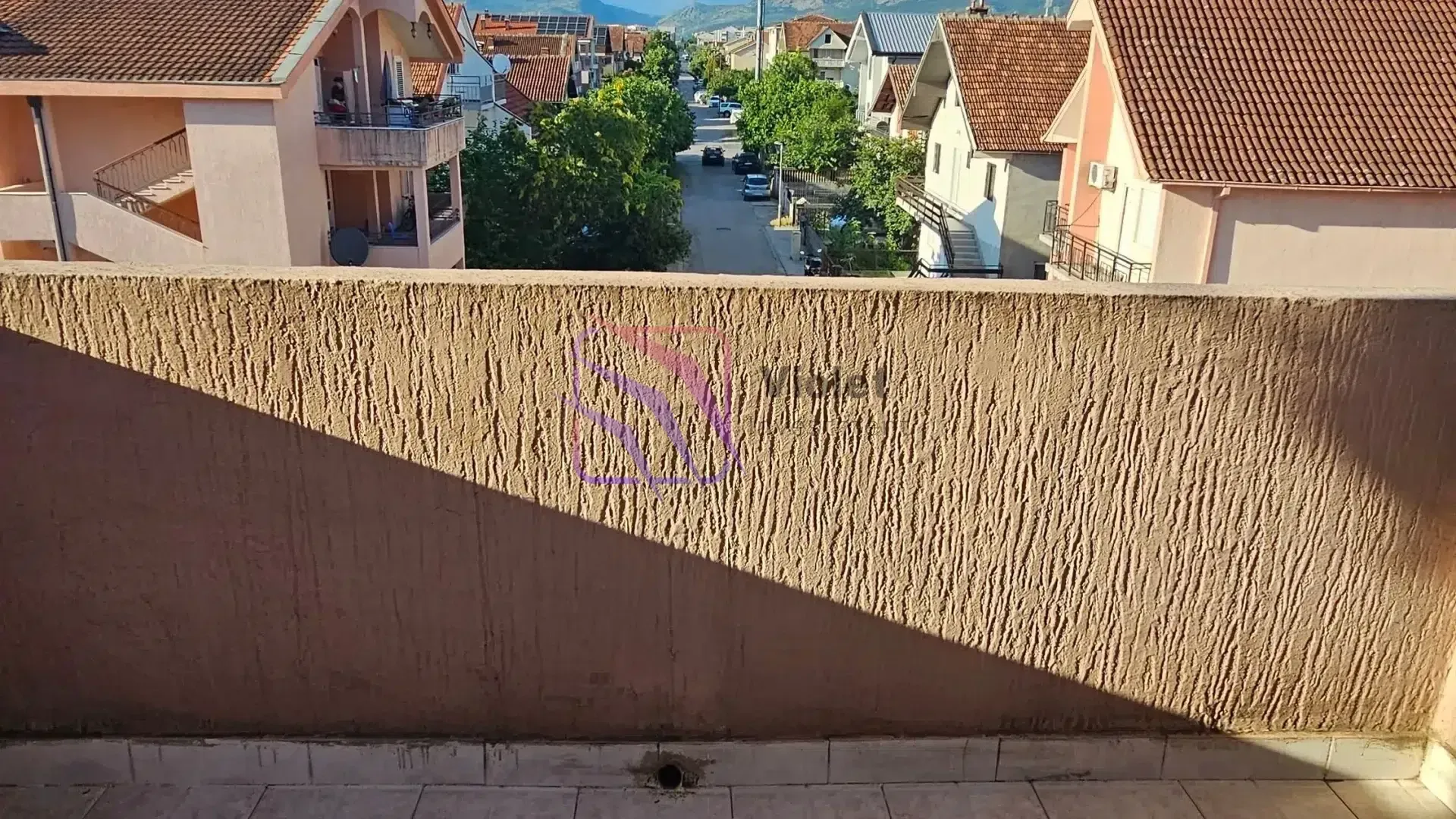 Pogled sa balkona na ulicu i okolne kuće.